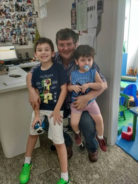 Dr. Ricardo com dois pacientes e a parede de fotos ao fundo